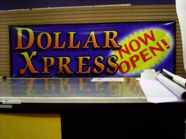 Sign reading "Dollar Xpress Now Open!" with a purple background and yellow and red text, on a store wall.