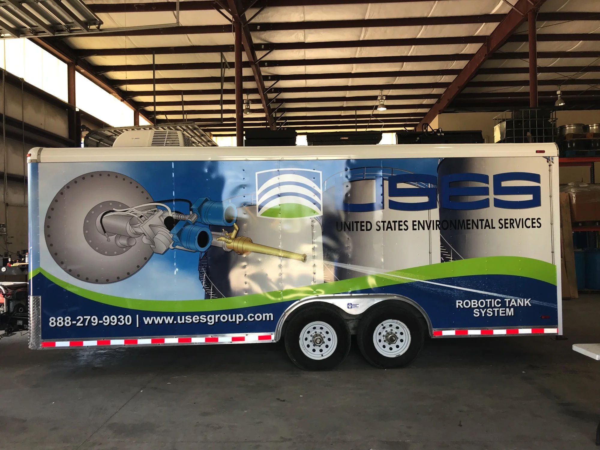 Mobile laboratory trailer with United States Environmental Services branding, featuring graphic designs related to robotic tank systems, parked inside a warehouse.