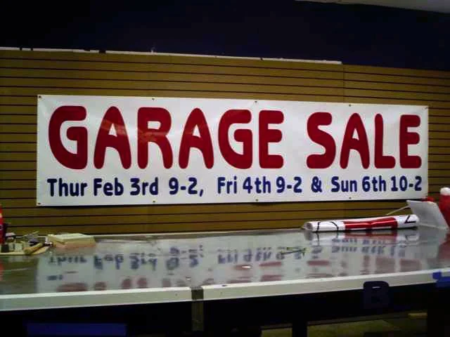 Sign for a garage sale with dates and times, placed on a wall above a table with some tools and materials.