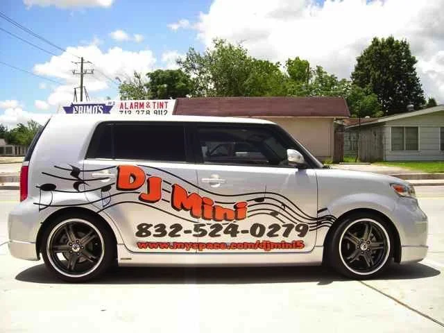 Silver SUV with promotional wrap for DJ Mini, featuring musical notes and contact information, parked on a street.