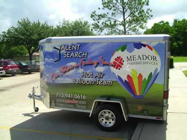 Mobile trailer display for Meador Staffing Services with a hot air balloon graphic and contact information in a parking lot.
