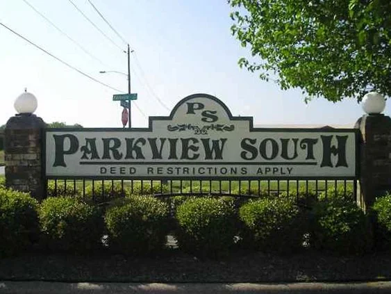 Sign that reads 'Parkview South' with a note that says 'Deed restrictions apply' beneath it, surrounded by bushes and a tree in the background.