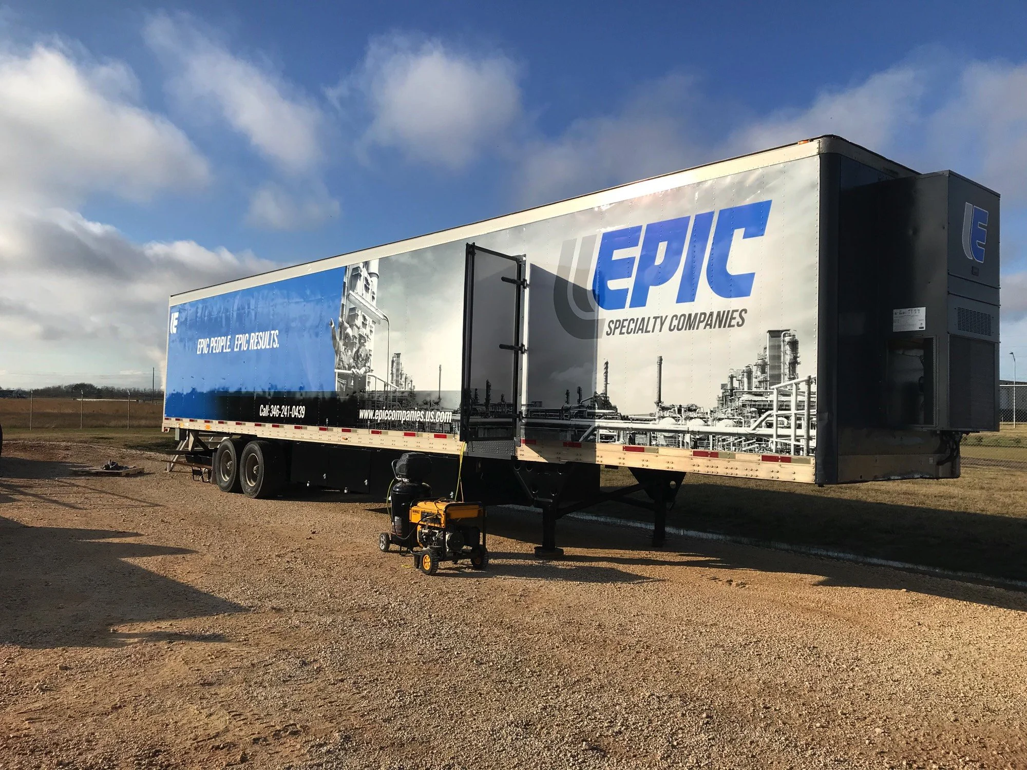 A large semi-truck trailer with blue and white branding for 'Epic Specialty Companies' is parked outdoors on a gravel surface under a partly cloudy sky. Equipment is visible underneath, and a small generator is in the foreground.