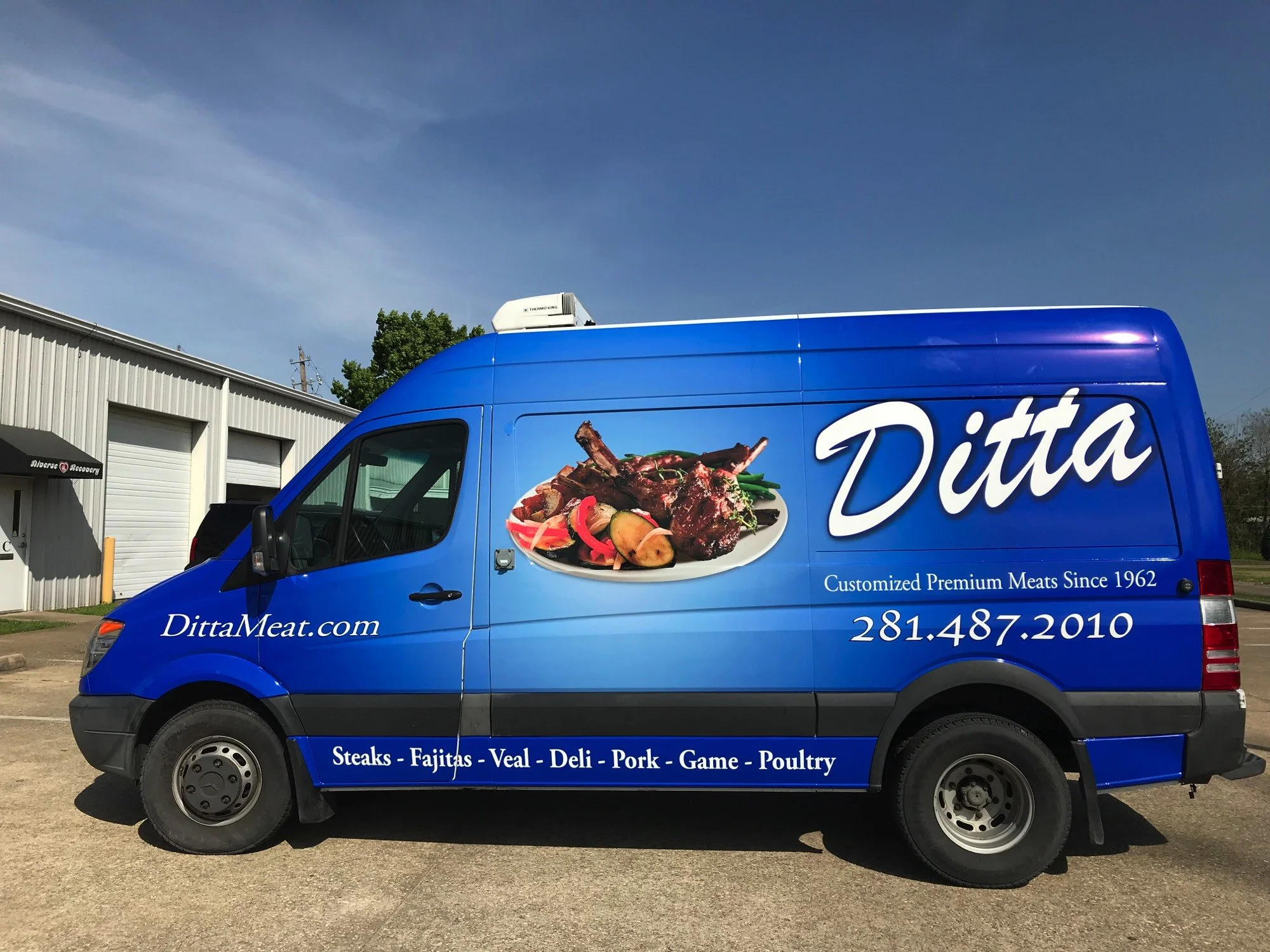 Blue food truck with a large image of grilled meat, vegetables, and the word 'Ditta' on its side, parked outside a warehouse, advertising various meats including steaks, fajitas, veal, deli, pork, game, and poultry.