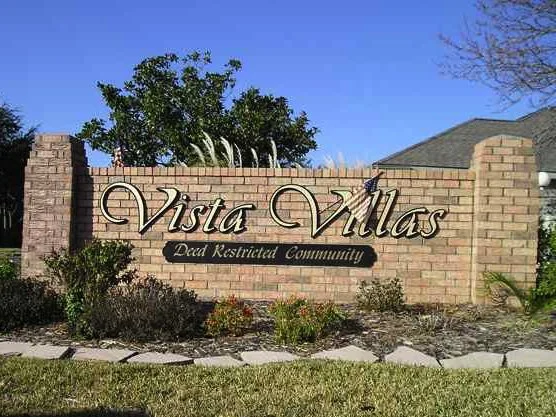 Sign that reads "Vista Villas" with a subtitle "Deed Restricted Community" next to landscaped plants and a blue sky in the background.