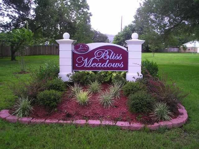 Sign for Bliss Meadows neighborhood surrounded by landscaped garden with bushes and grass.