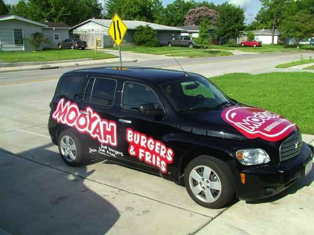 Black car with Mooyah Burgers & Fries advertisement, parked on driveway in a residential neighborhood.