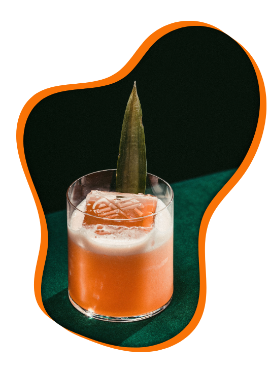 A pink cocktail with a pineapple slice garnish in a short glass with ice against a black and green background.