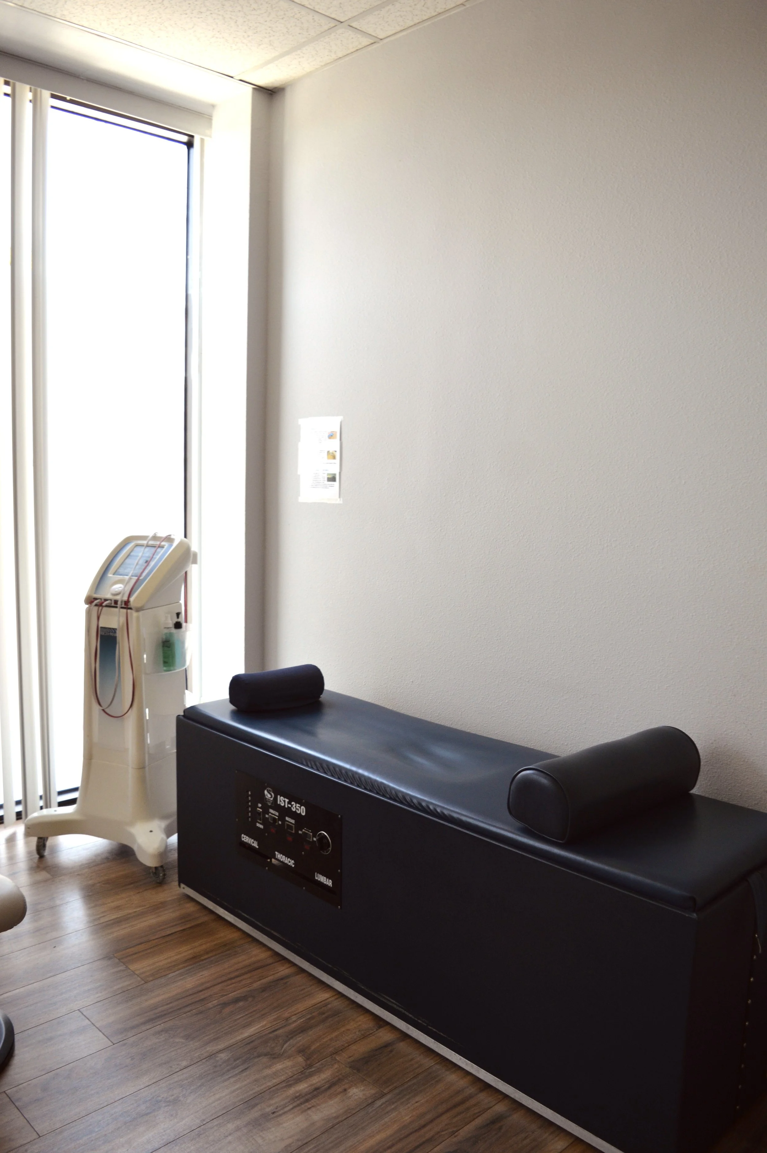 Medical treatment room with examination table, medical equipment, and a window with vertical blinds.