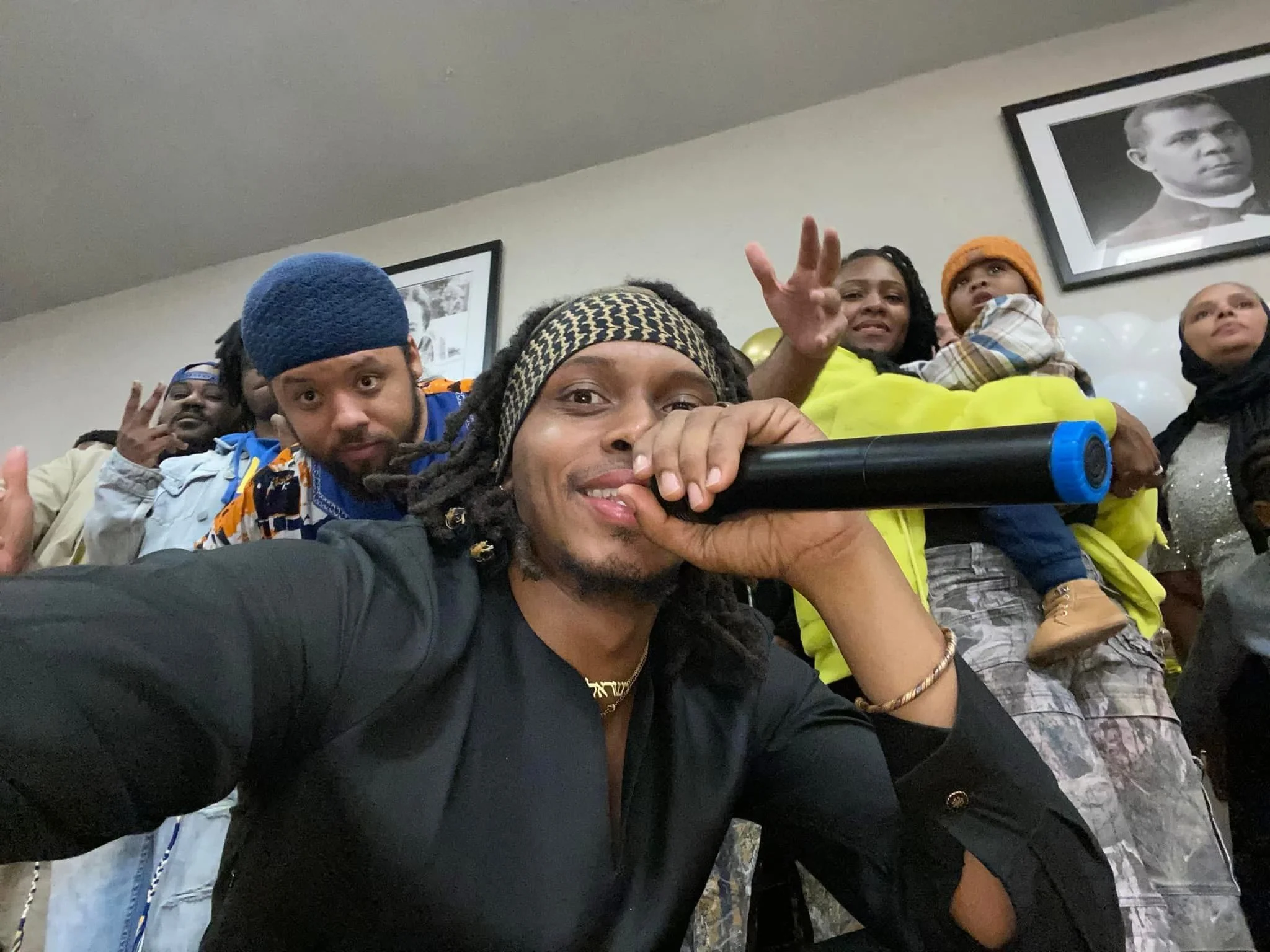 Group of diverse (Israelites) young adults and children taking a selfie together indoors, with framed black and white photographs on the wall behind them. New Legacy Initiative. New Legacy, Inc.