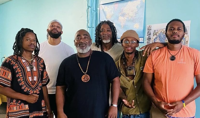 A group of seven people (Israelites) standing together indoors, posing for a photo, with a blue wall and a window in the background. New Legacy Initiative. New Legacy, Inc.