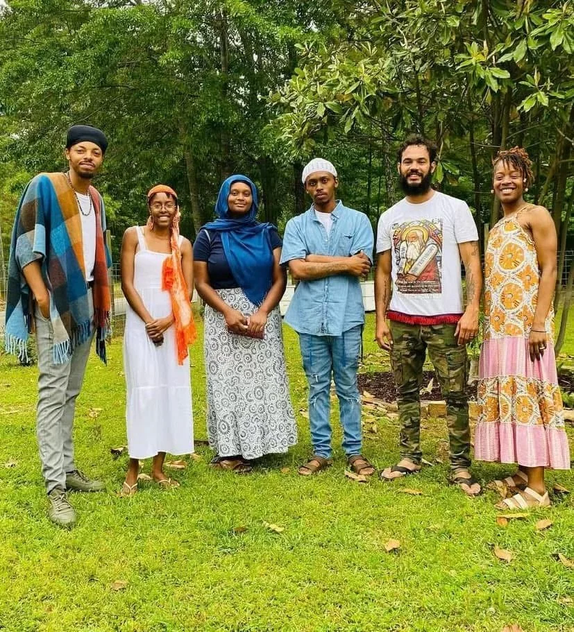 Group of seven (Israelites) diverse people standing outdoors on grass with trees in the background, smiling. New Legacy Initiative. New Legacy, Inc.