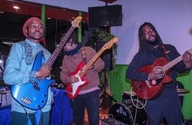 Three Israelite musicians playing guitars on stage with purple and green lighting. New Legacy Initiative. New Legacy, Inc.