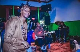 An Israelite man smiling at a live music event with musicians playing instruments in the background. New Legacy Initiative. New Legacy, Inc.