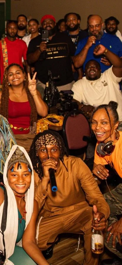 Group photo of diverse people (Israelites) smiling and making gestures at a social gathering or party, with some holding drinks and others wearing accessories. New Legacy Initiative. New Legacy, Inc.