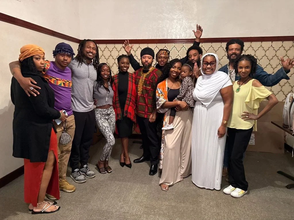 A group of diverse people (Israelites) posing together indoors, some with their arms raised or around each other, smiling at the camera. New Legacy Initiative. New Legacy, Inc.