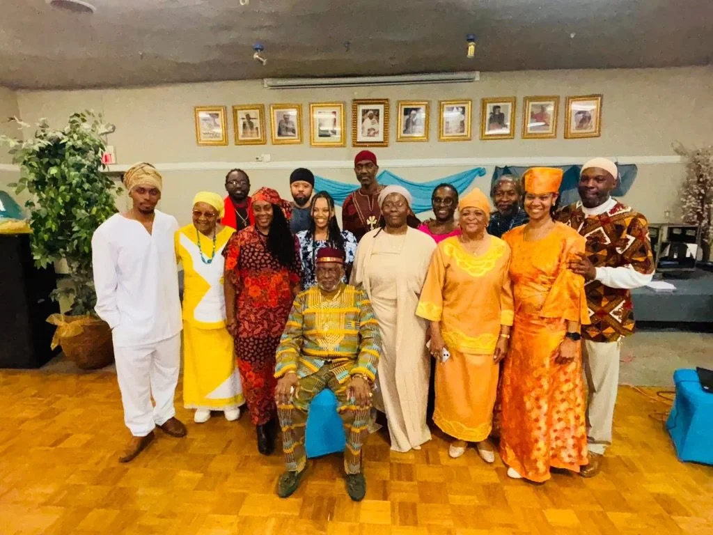 Group of people (Israelites) dressed in traditional and colorful clothing posing together indoors, with framed photos on the wall behind them. New Legacy Initiative. New Legacy, Inc.