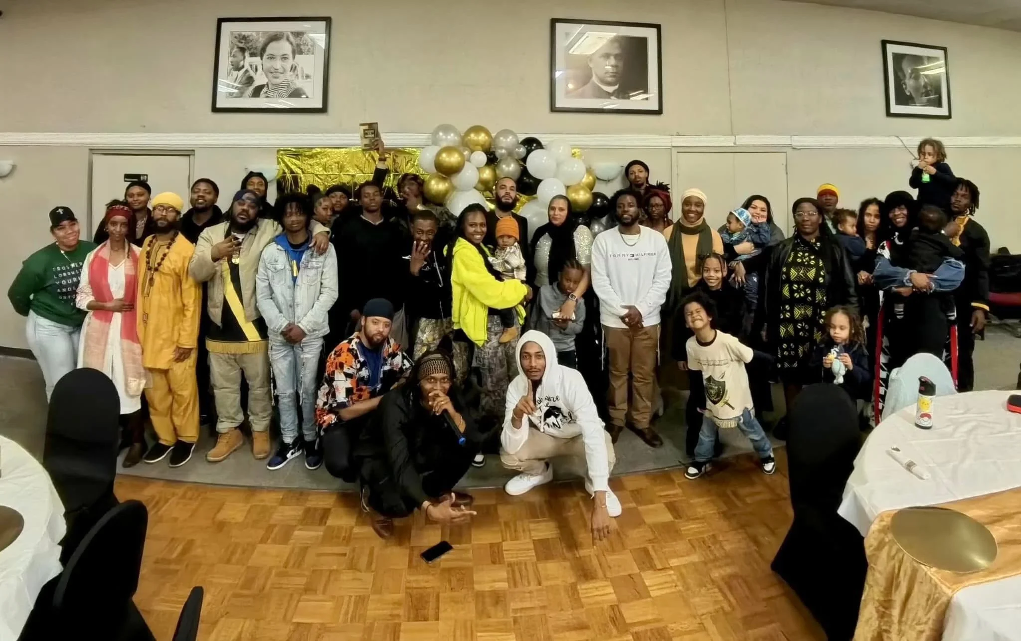 Group of people (Israelites) posing for a photo at an indoor event with a backdrop of gold and black balloons. New Legacy Initiative. New Legacy, Inc.