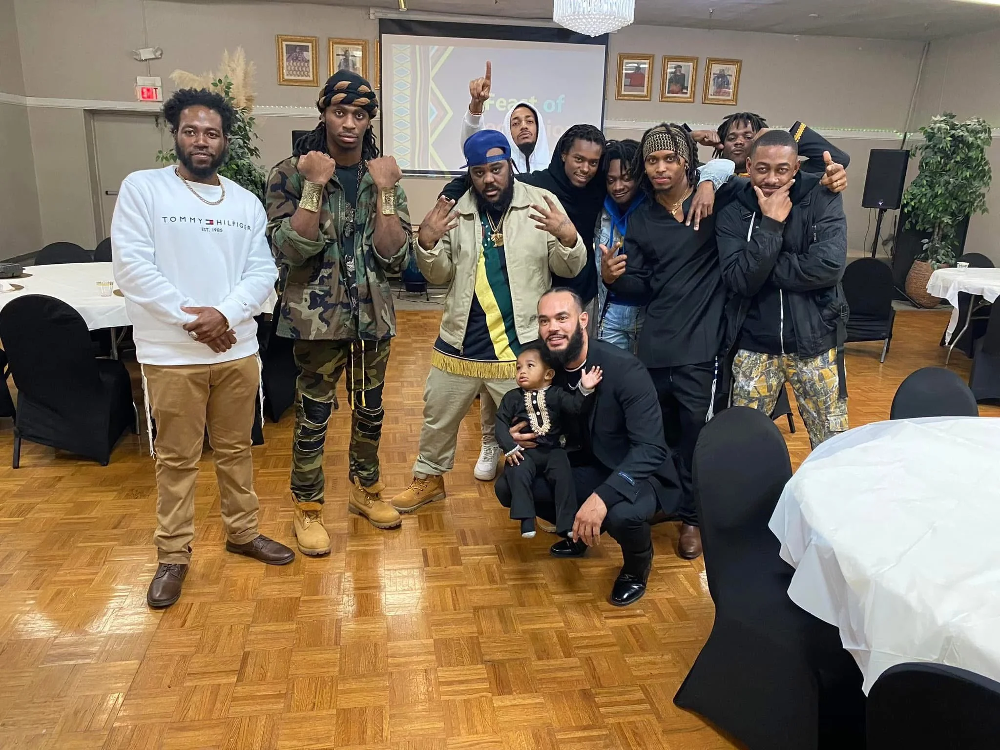 A group of ten people (Israelites), including children, gathered in a banquet hall, posing for a group photo. The setting has round tables with white tablecloths, black chairs, and some decorative plants. New Legacy Initiative. New Legacy, Inc.