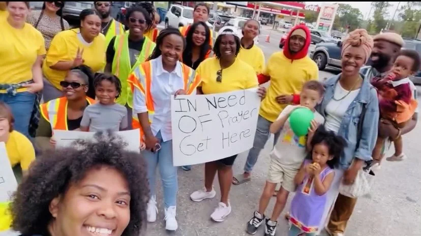 Group of diverse people (Israelites), including children and adults, gathered outdoors, holding signs demanding prayer and support. New Legacy Initiative. New Legacy, Inc.