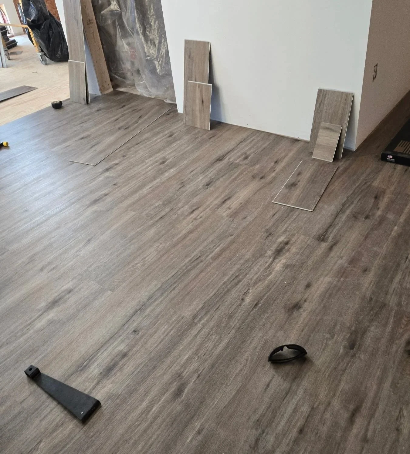 Installation of wood-like flooring tiles on a room floor with tools and tiles leaning against the wall.