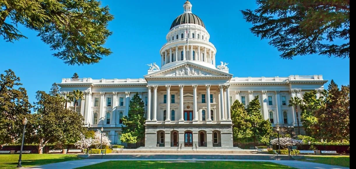 The California State Capitol building in Sacramento, featuring neoclassical architecture with a large dome, columns, and surrounded by trees and a well-maintained lawn.