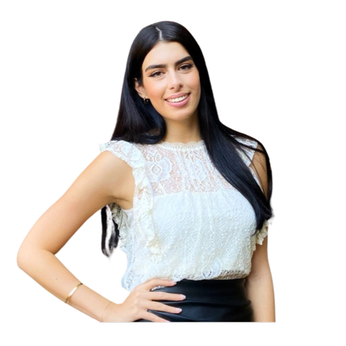 A young woman with long dark hair, smiling, wearing a white lace sleeveless blouse and black skirt, posing with one hand on her hip.
