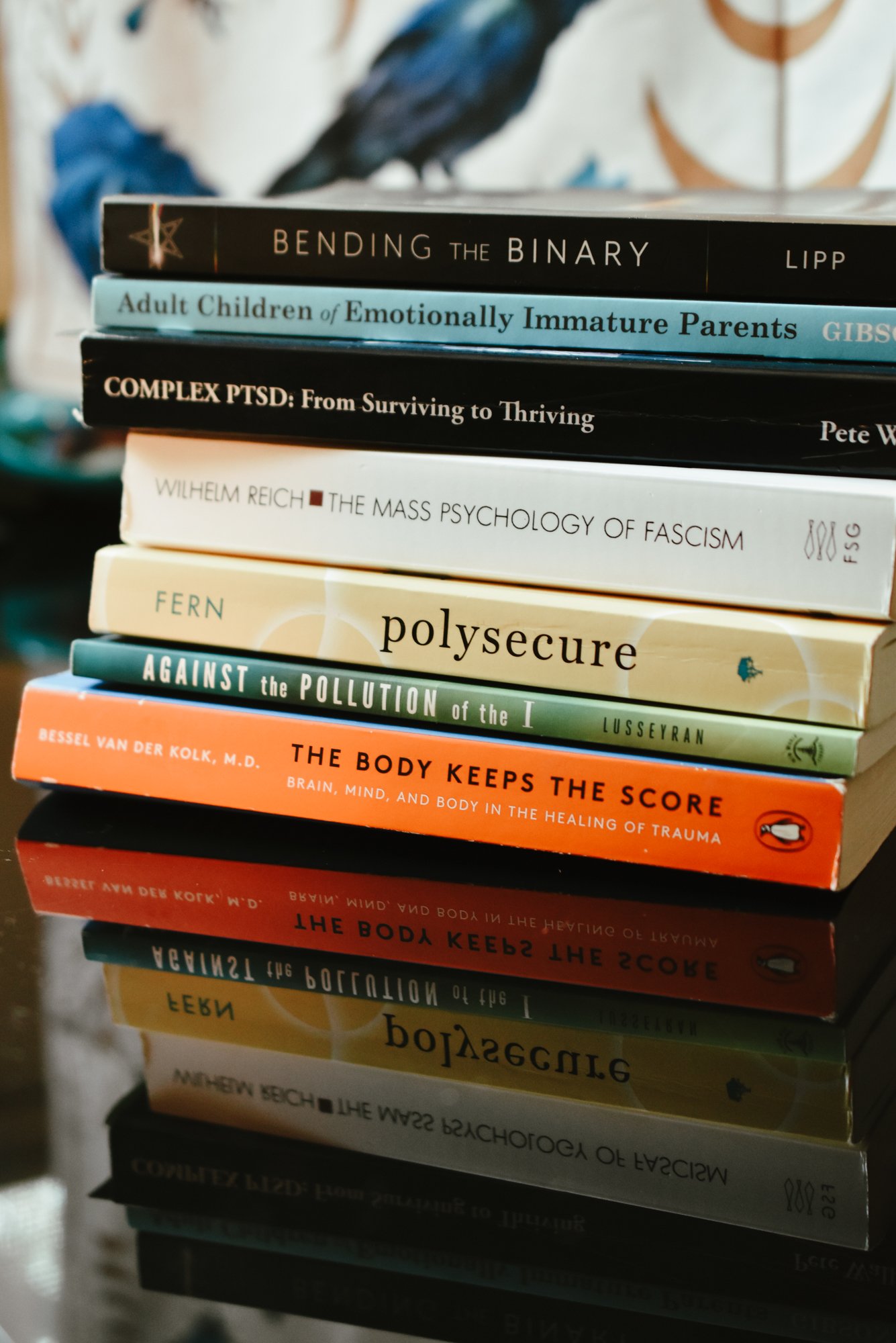 Stack of therapy and spiritual seeking books on a reflective surface with a blurred background scarf of blue birds.