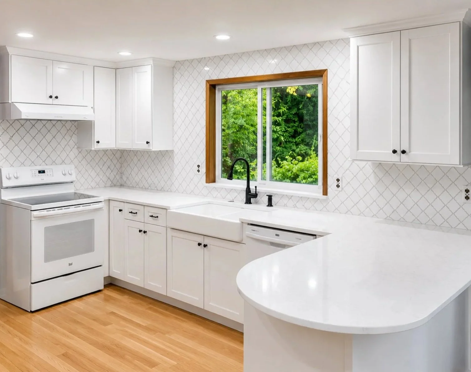 Modern white kitchen with a window showing greenery outside, black faucet, white appliances, and light hardwood flooring.
