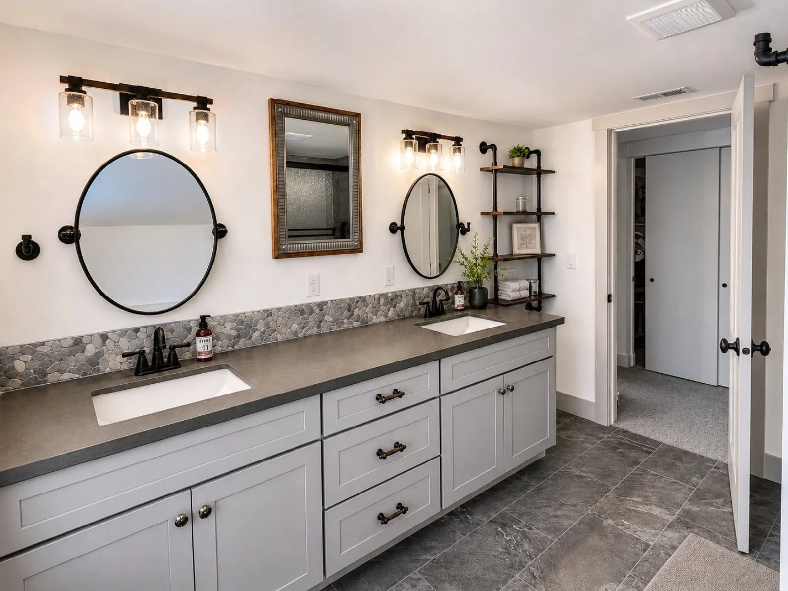 Modern bathroom with double vanity, two oval mirrors, pebble tile backsplash, wall-mounted lights, and open shelving with towels and decor.