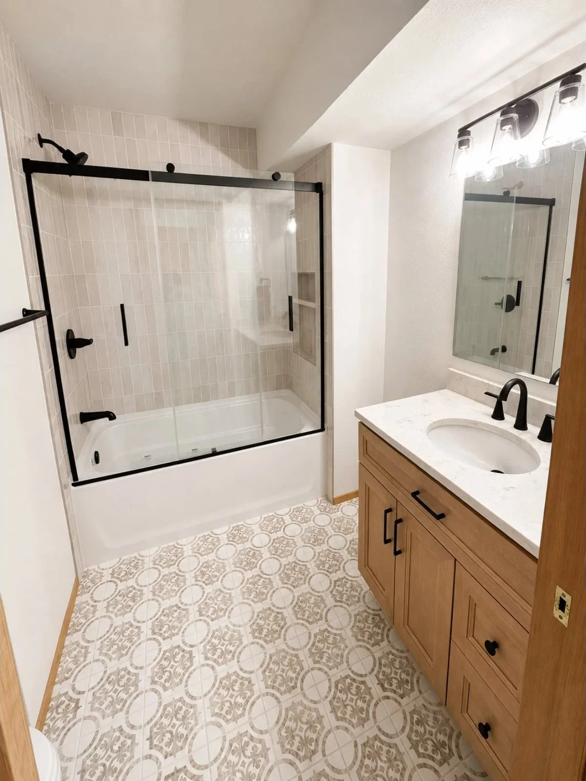 Bathroom with a glass-enclosed shower, a wooden vanity with a marble countertop, and patterned tile flooring.