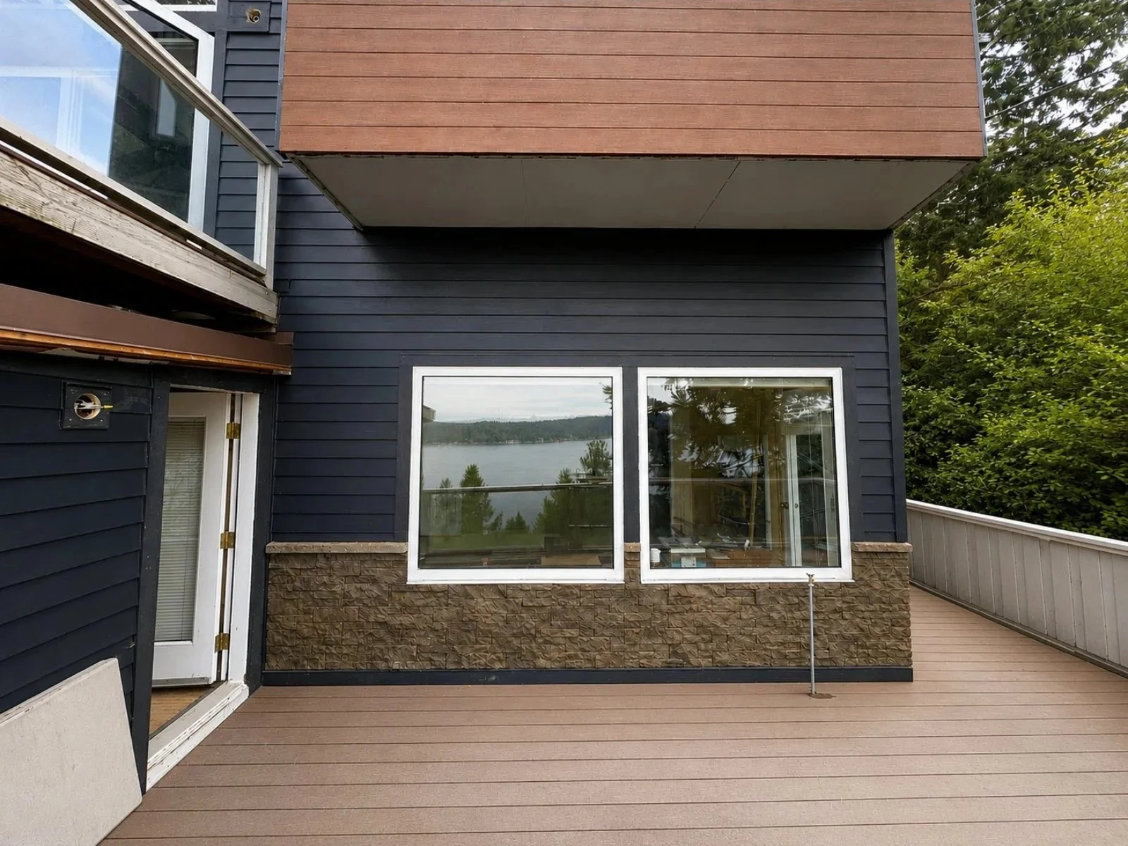 Newly sided modern house with horizontal black siding, white-framed window, brown stone lower wall, and sliding glass door with trees in the background.