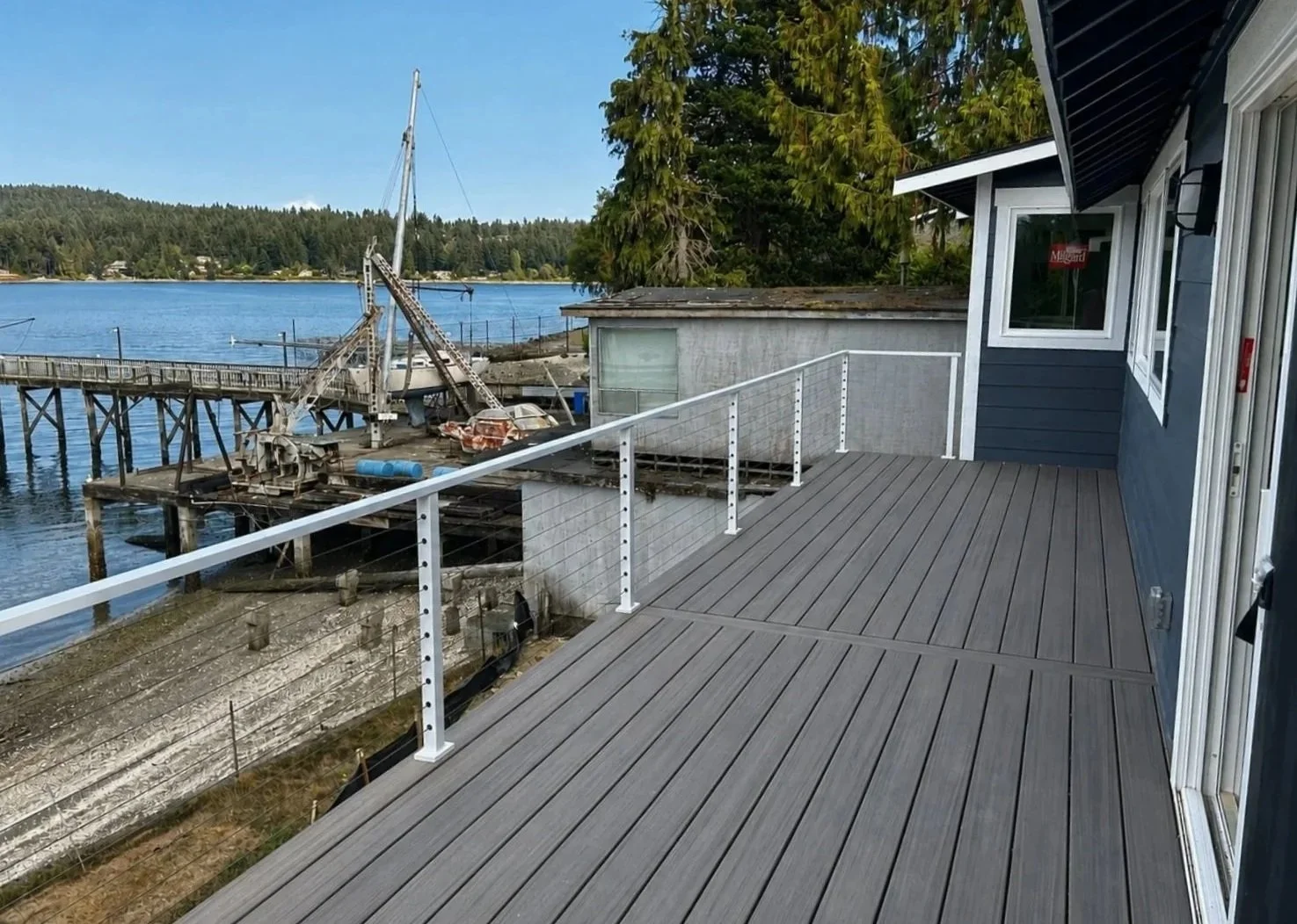 View of a newly built composite deck with a metal railing, overlooking a body of water with an old, abandoned pier and boat in the background. 