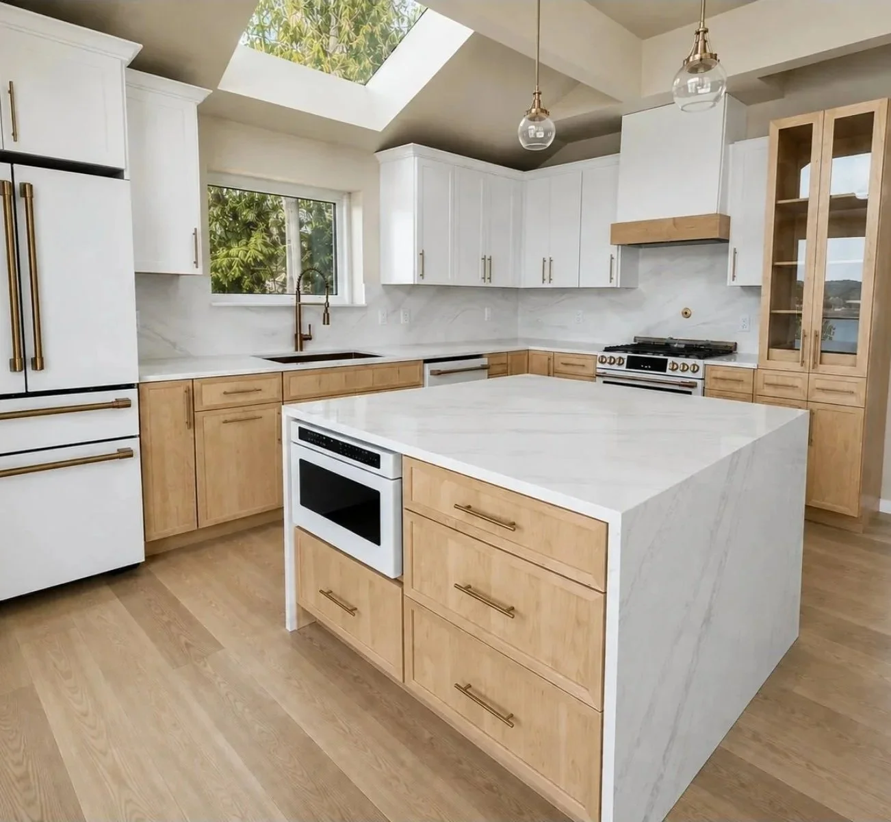 Modern kitchen with white and light wood cabinetry, white marble countertops, a kitchen island, stainless steel appliances, a skylight, and pendant lighting.