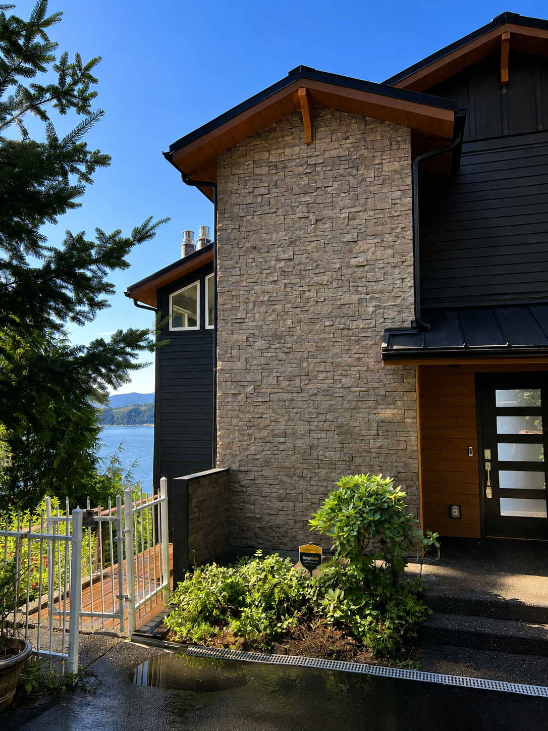 Modern house with newly installed stone facade, black siding, metal roofing, and new gutters with a landscaped entrance, and mountain views.