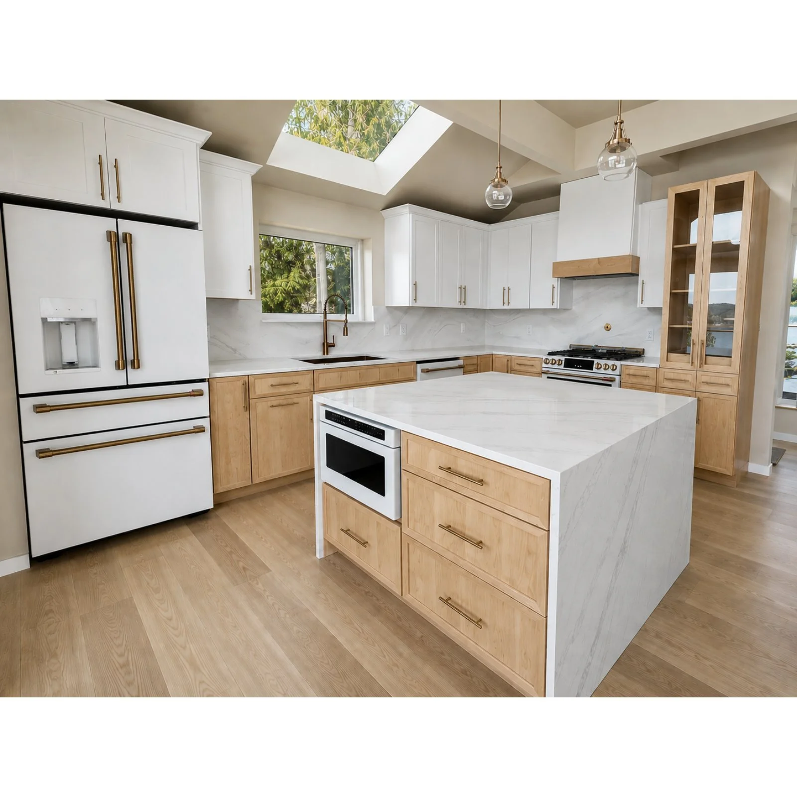 Modern kitchen with white and light wood cabinetry, a white marble island, stainless steel appliances, pendant lighting, a skylight, and a window showing greenery outside.