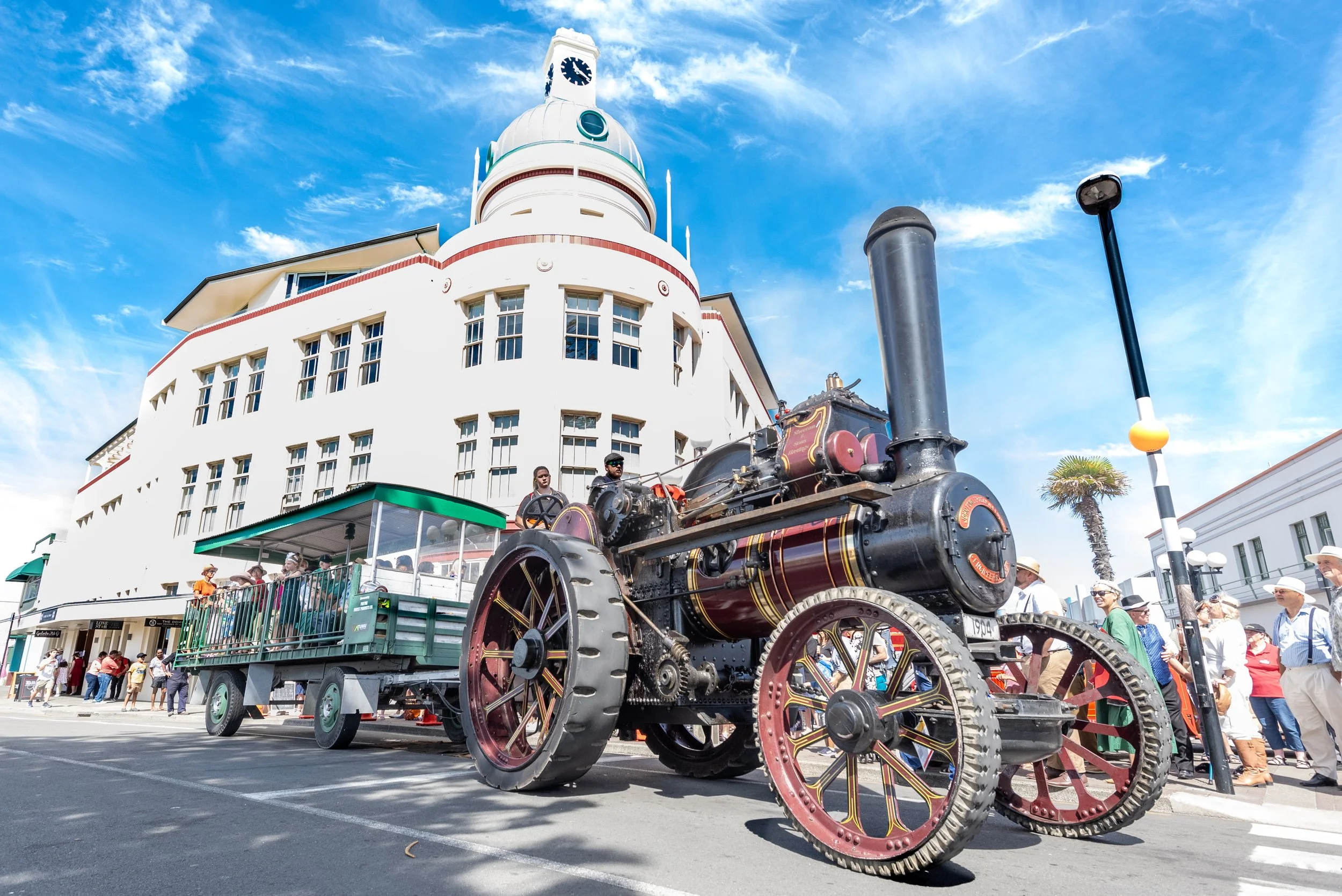 Vintage steam locomotive on display with people gathered around at an outdoor event under a partly cloudy sky.