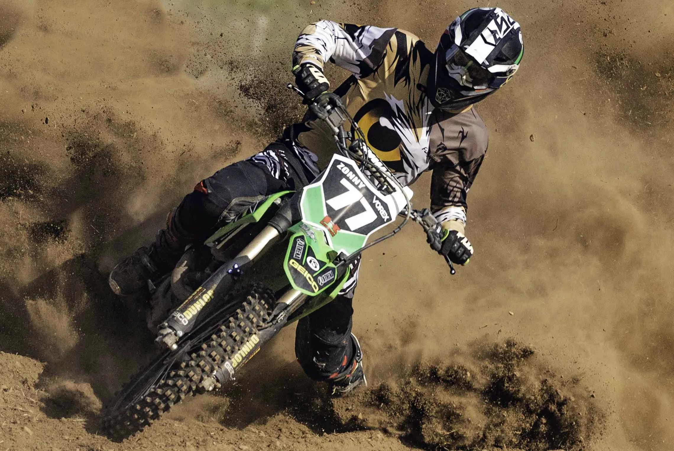 A dirt bike rider wearing a helmet and gear, riding on a dirt track, kicking up dust.