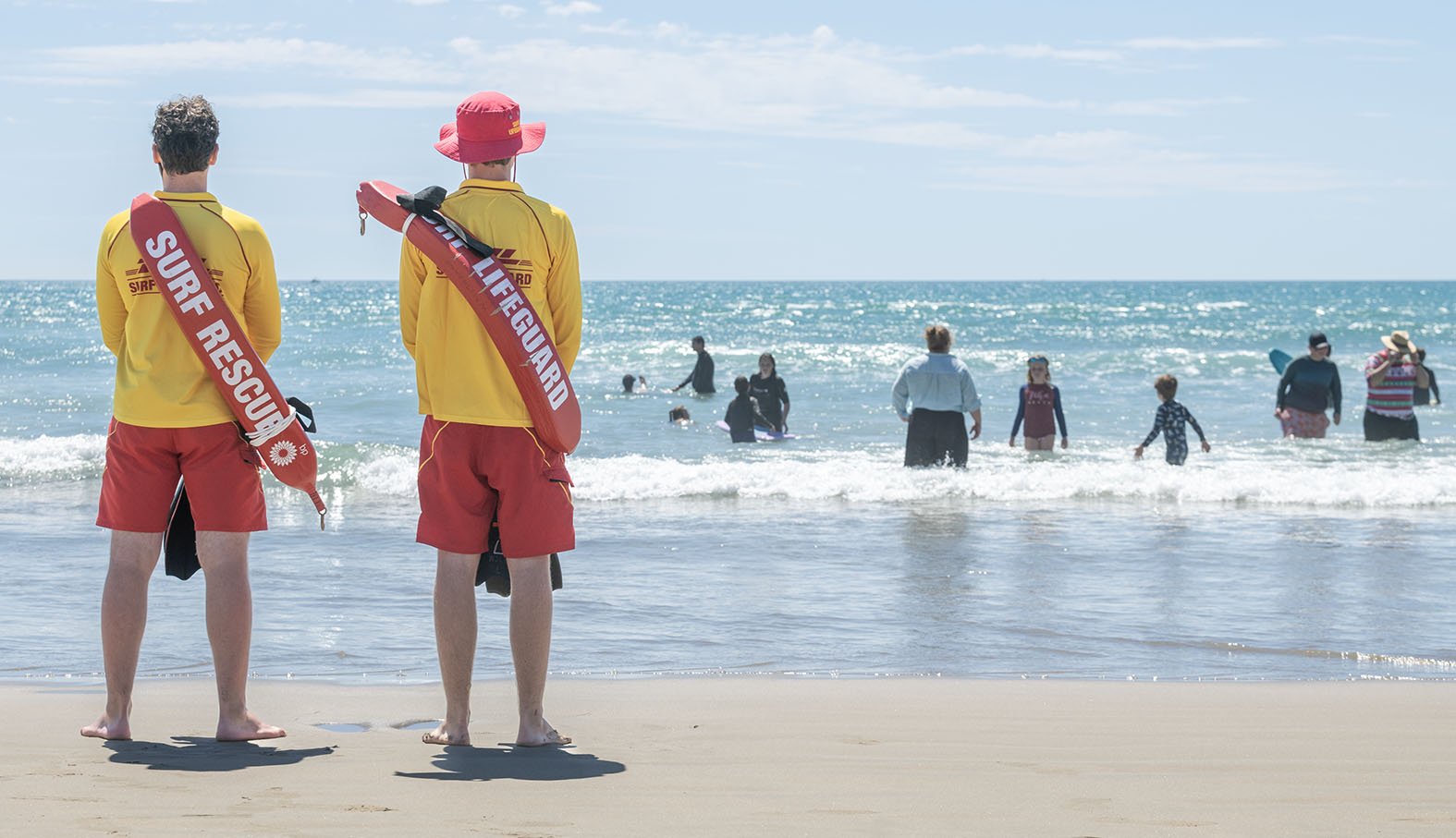 Two lifeguards standing on the beach watching over people swimming in the ocean.