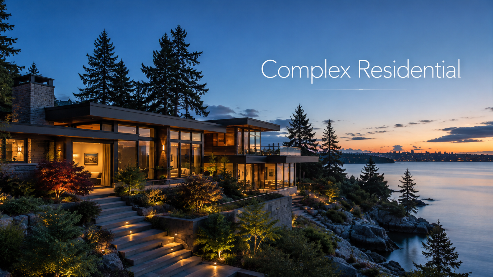 Luxury modern house on a hillside overlooking the water at sunset with trees and Seattle skyline in the background.
