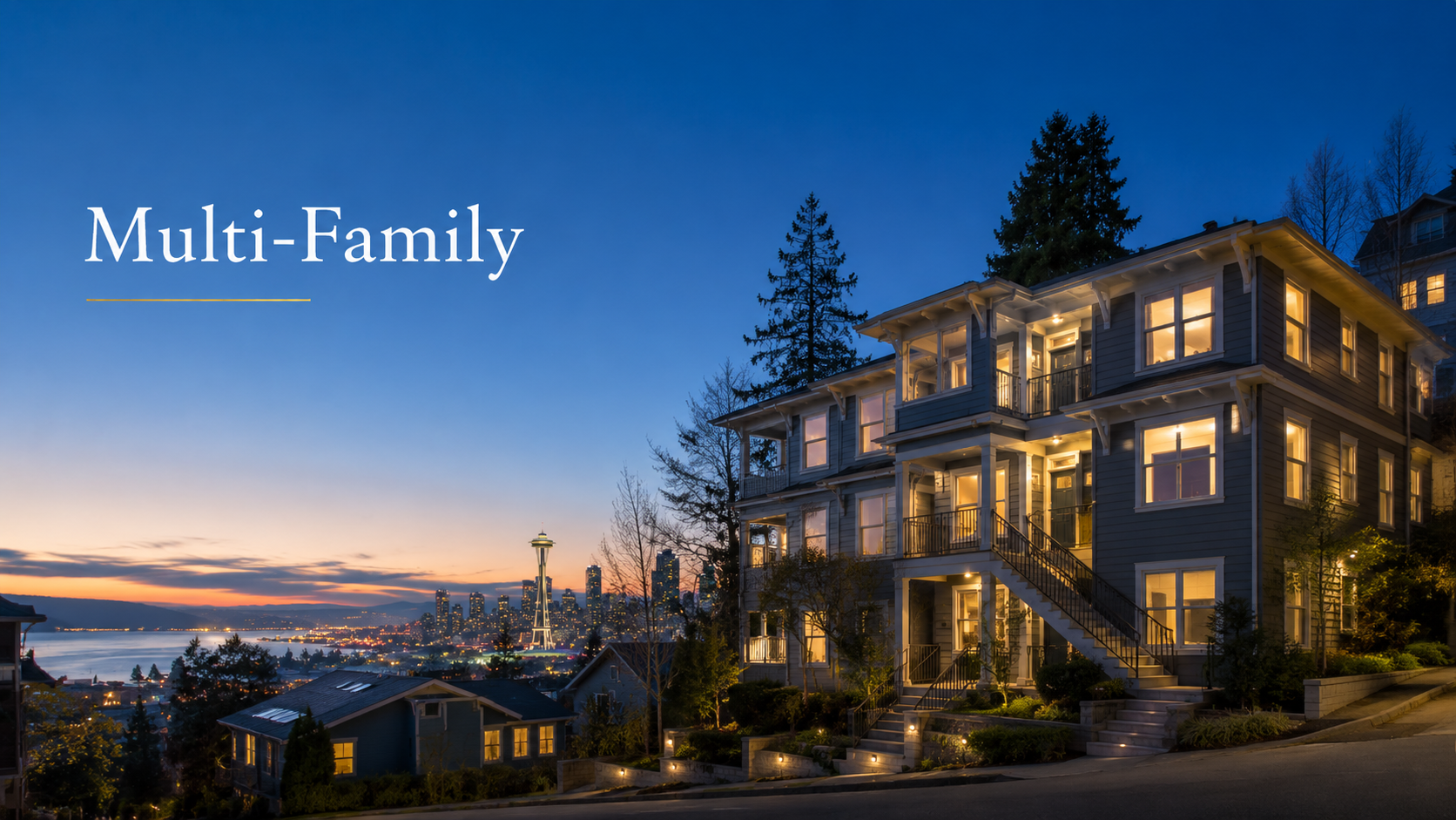 A multi-family house on a hillside at dusk with the Seattle skyline and Space Needle in the background, illuminated with warm interior lights.