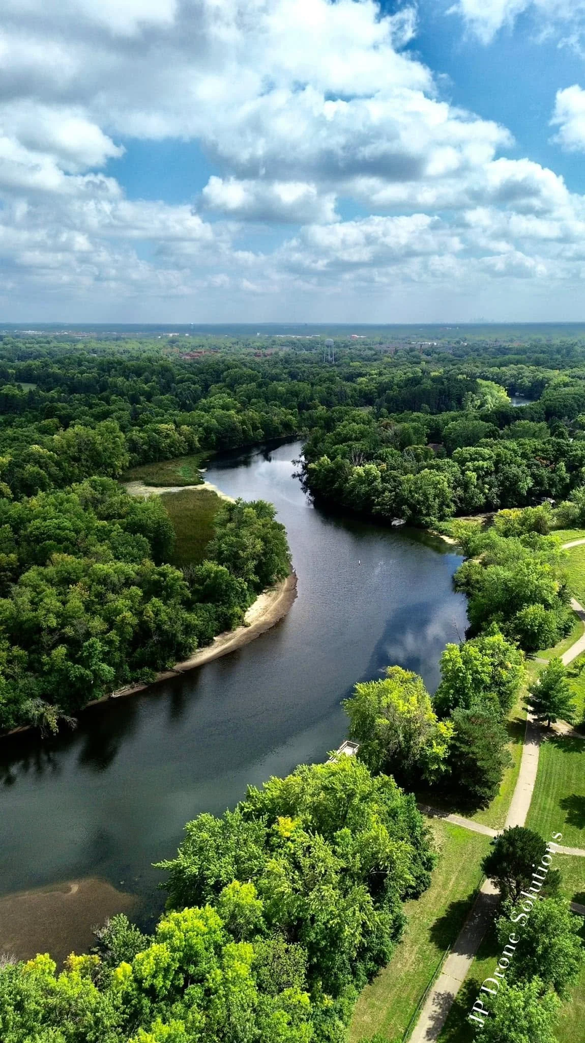 Aerial view of a winding river surrounded by lush green trees and grassy areas under a partly cloudy sky.