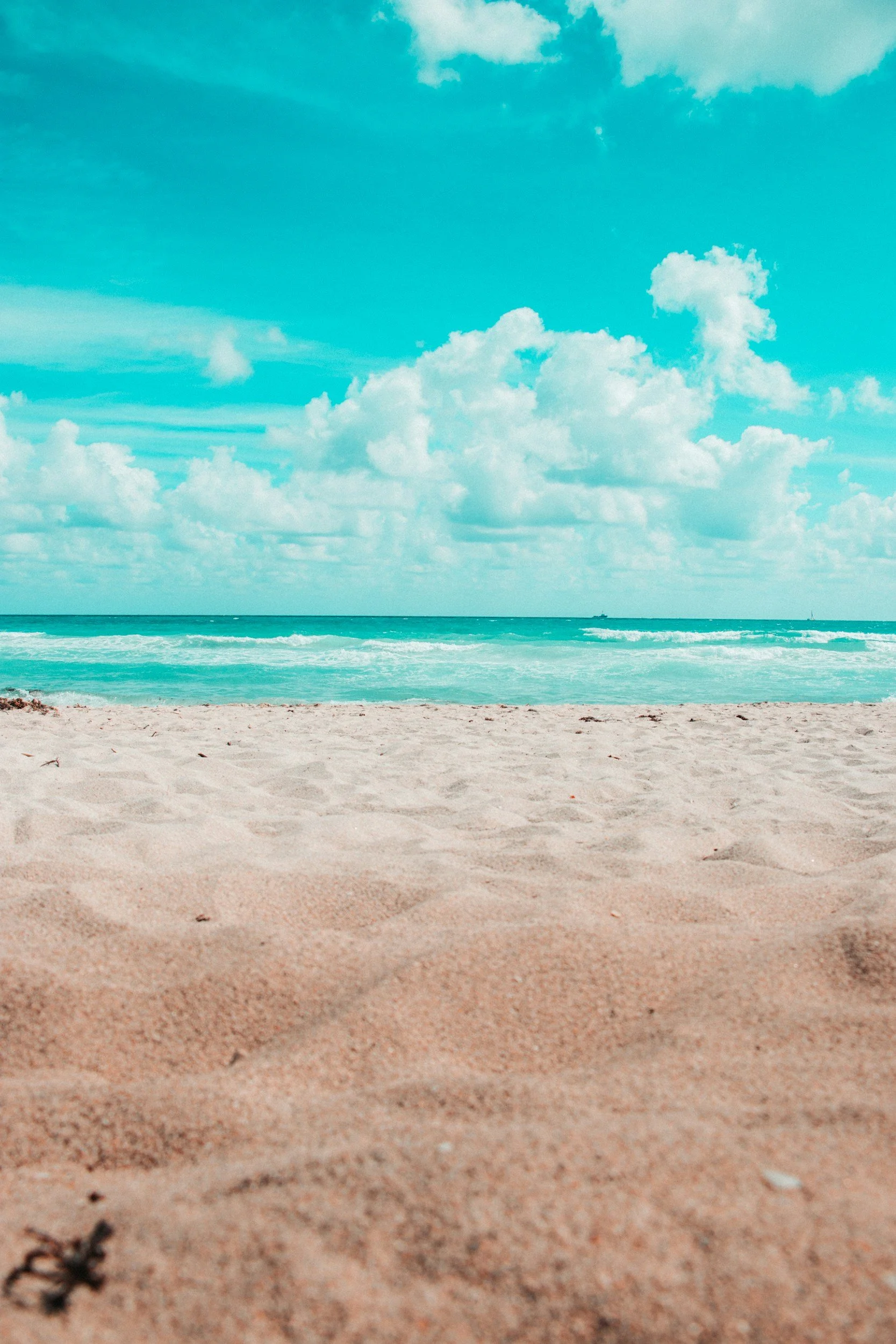 Sandy beach with ocean waves and a partly cloudy sky.