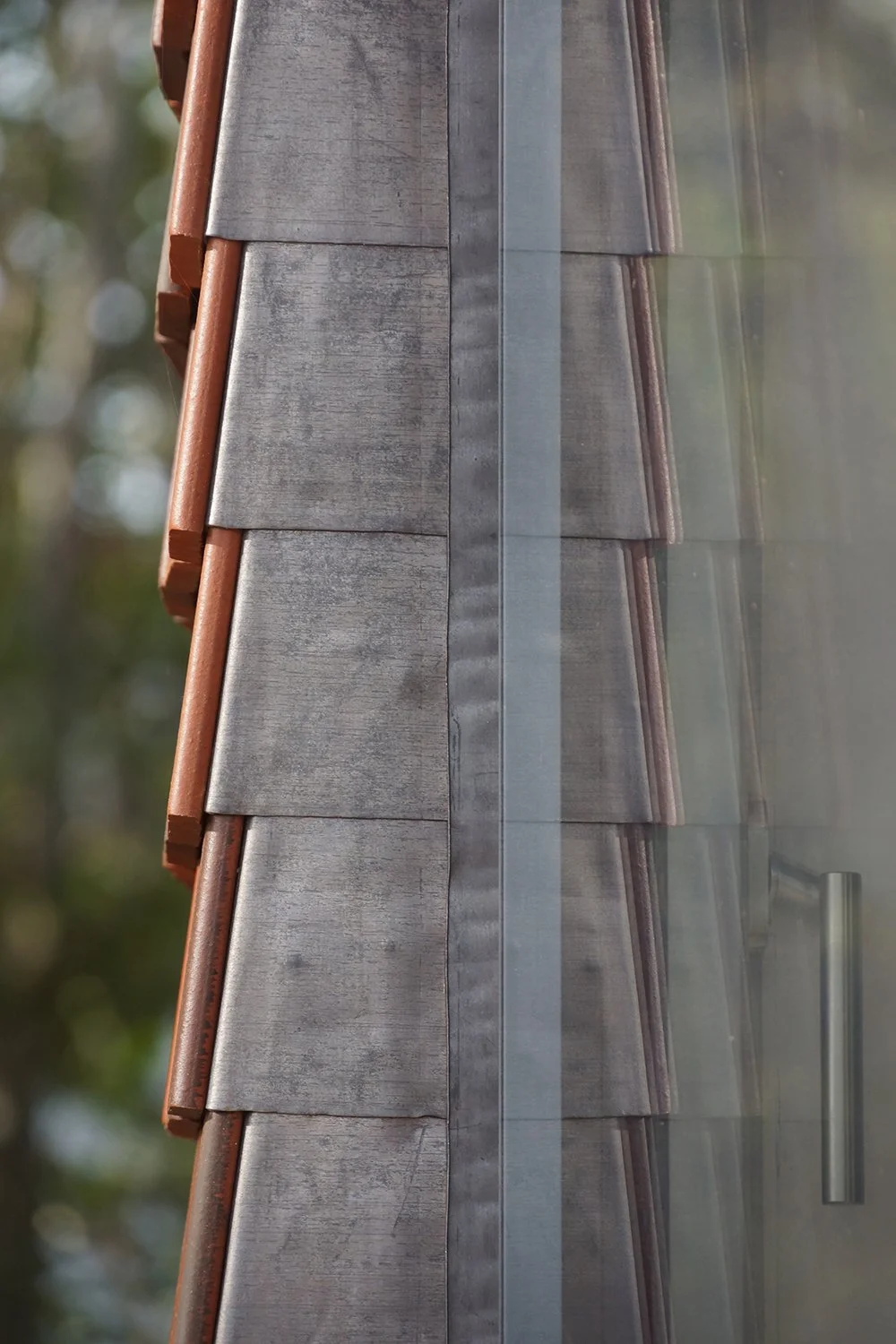 Close-up detail of lead detailing wrapping the window reveal in the clay shingle facade.
