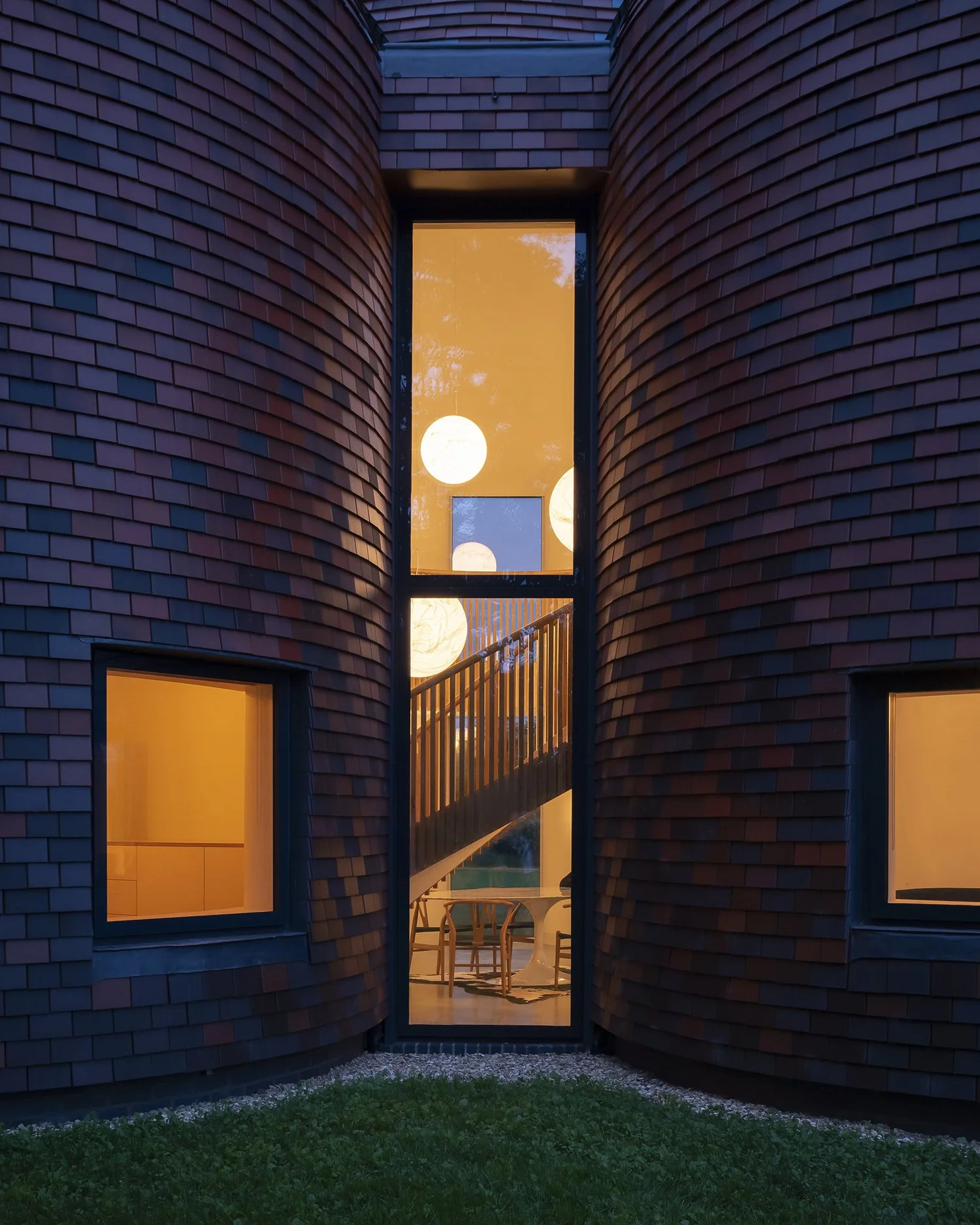 Lucy Moroney Project Architect, exterior view through roundels at twilight with a warm interior glow and glimpse of sculptural stair