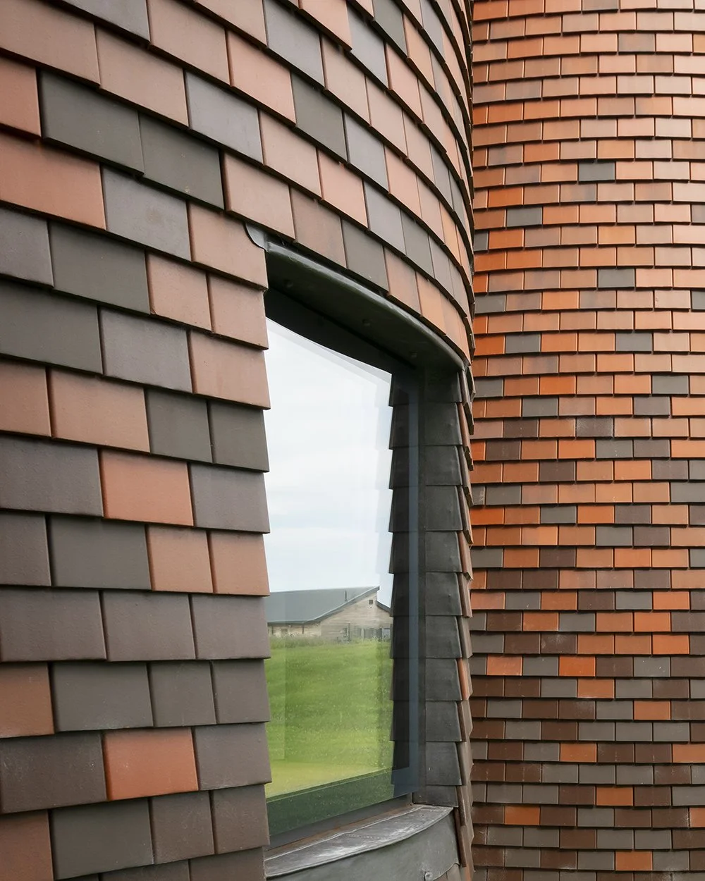 Exterior view of window cutting through the clay shingle facade, with lead detailing wrapping the reveal.