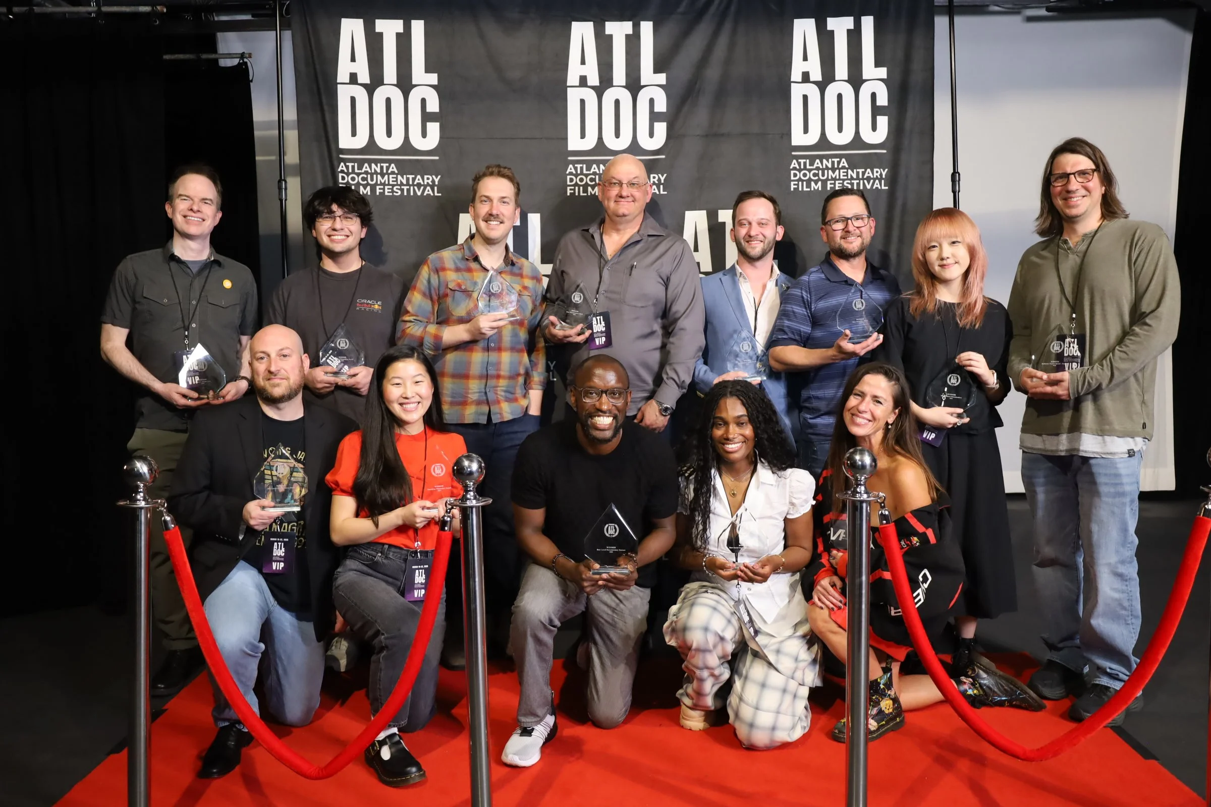 Group of people at the Atlanta Documentary Film Festival, some holding awards, standing behind red velvet rope with a black backdrop displaying the festival's logo.