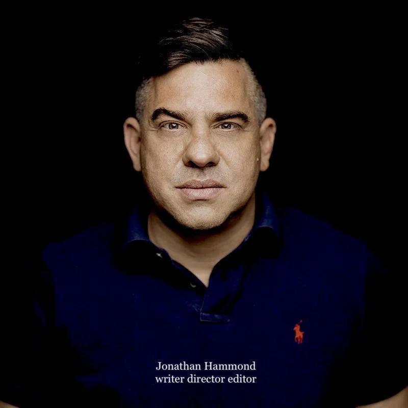 Portrait of a man with short dark hair, wearing a dark blue polo shirt with a red Ralph Lauren logo, against a black background.