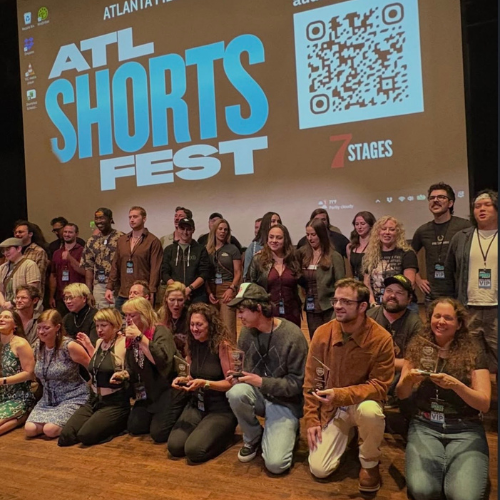 Group of people at ATL Shorts Fest on stage holding awards, with a large screen behind them displaying the event logo, QR code, and stages text.