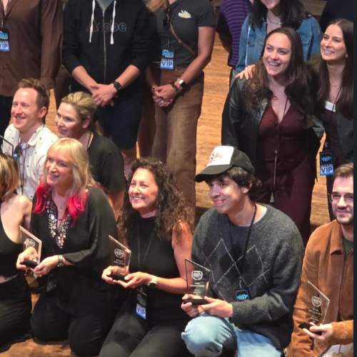 Group of people on stage during an award ceremony, some holding plaques, smiling, and wearing VIP badges.